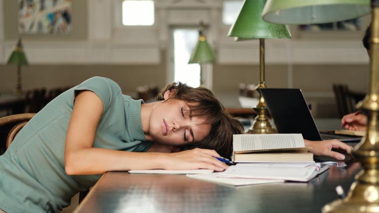 Female student studying, sleeping with head on table in library